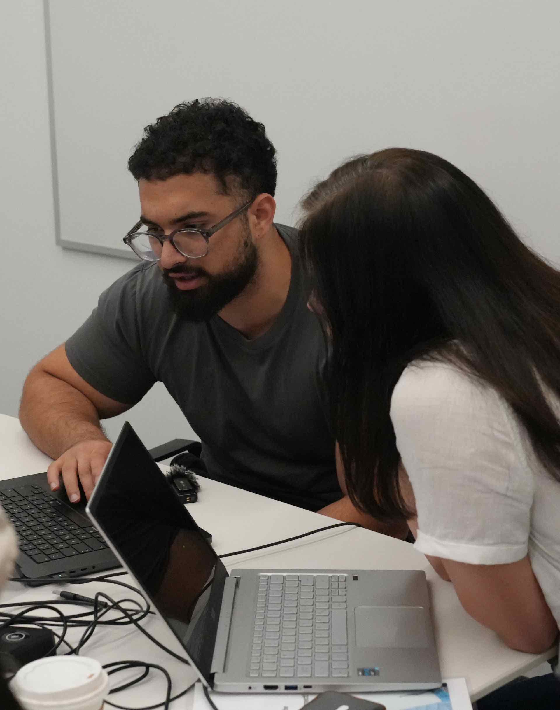 An instructor leaning in to help an attendee at her laptop during a Zero to Agent working session